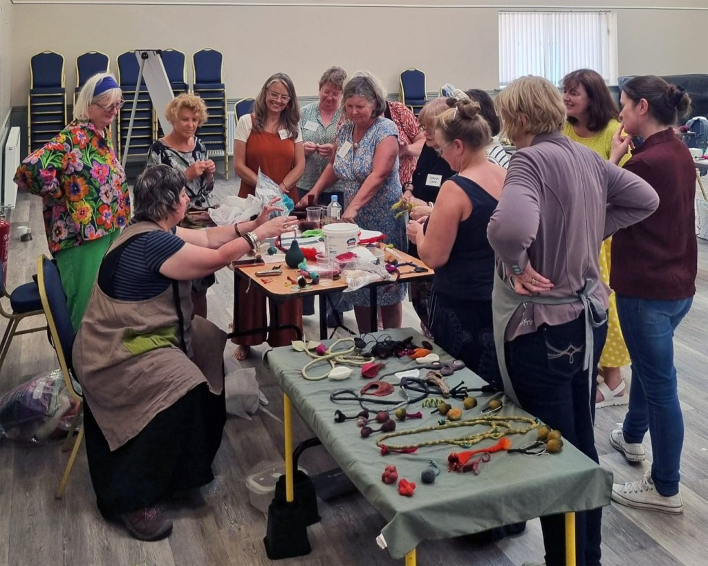 Pam demonstrating. In the foreground are sample pieces of felted jewellery that she has created.